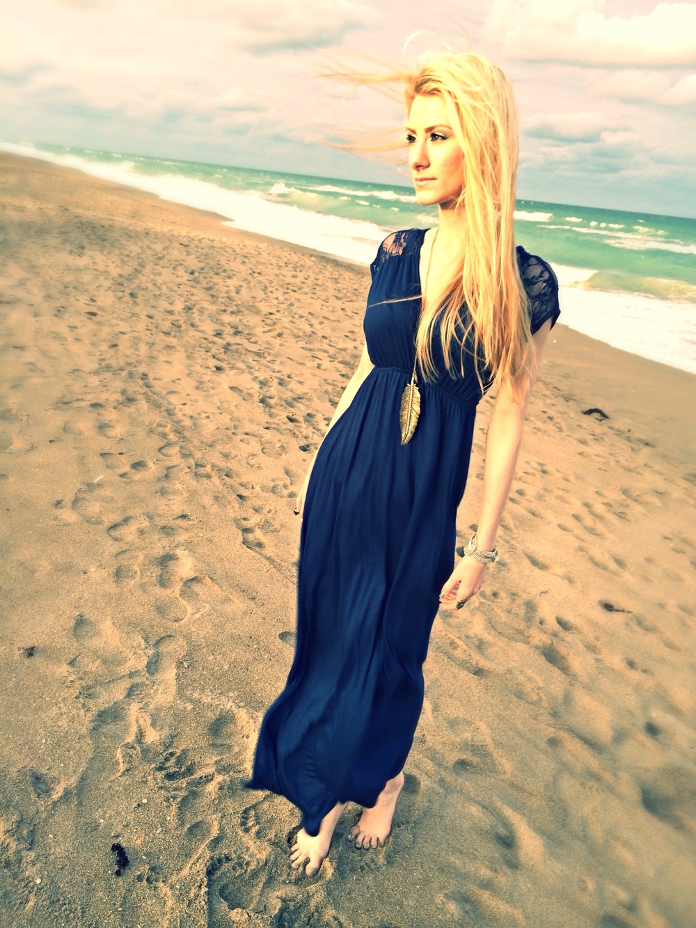 North Carolina fashion and lifestyle blogger Jessica Linn wearing a navy blue maxi dress, silver sandals, an da feather pendant necklace on a beach in Florida.