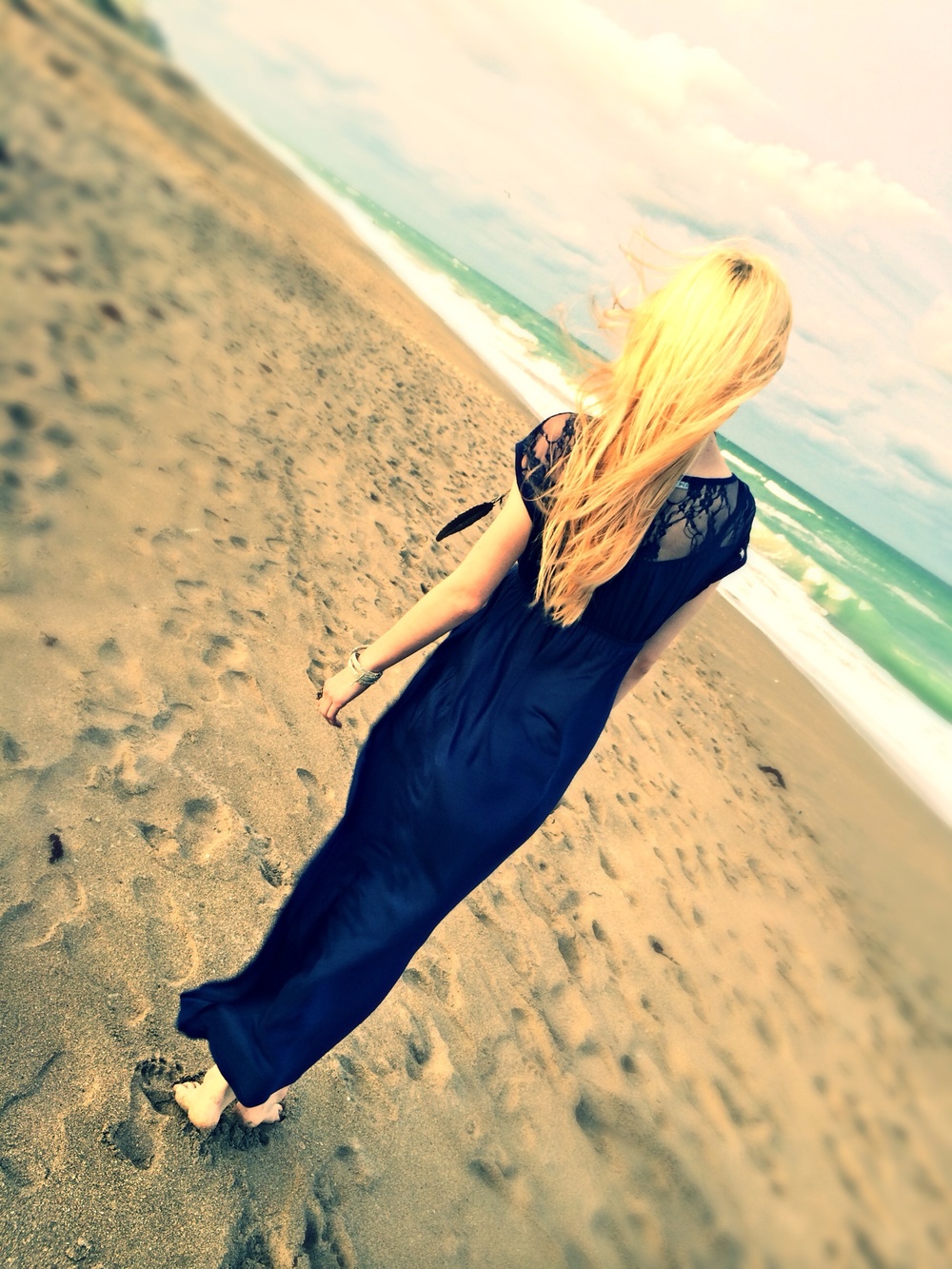 North Carolina fashion and lifestyle blogger Jessica Linn wearing a navy blue maxi dress, silver sandals, an da feather pendant necklace on a beach in Florida.