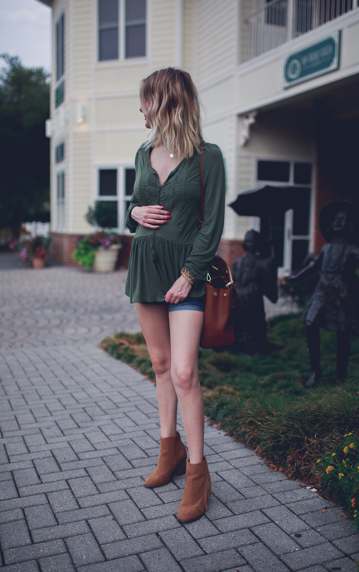 Lifestyle and fashion blogger Jessica Linn from Linn Style wearing a flow green peasant blouse from Express, maternity shorts, forever21 faux suede fringed booties, a brown Micheal kore purse and a necklace from CY Design Studio in Downtown Cary North Carolina. Maternity and pregnancy fashion.