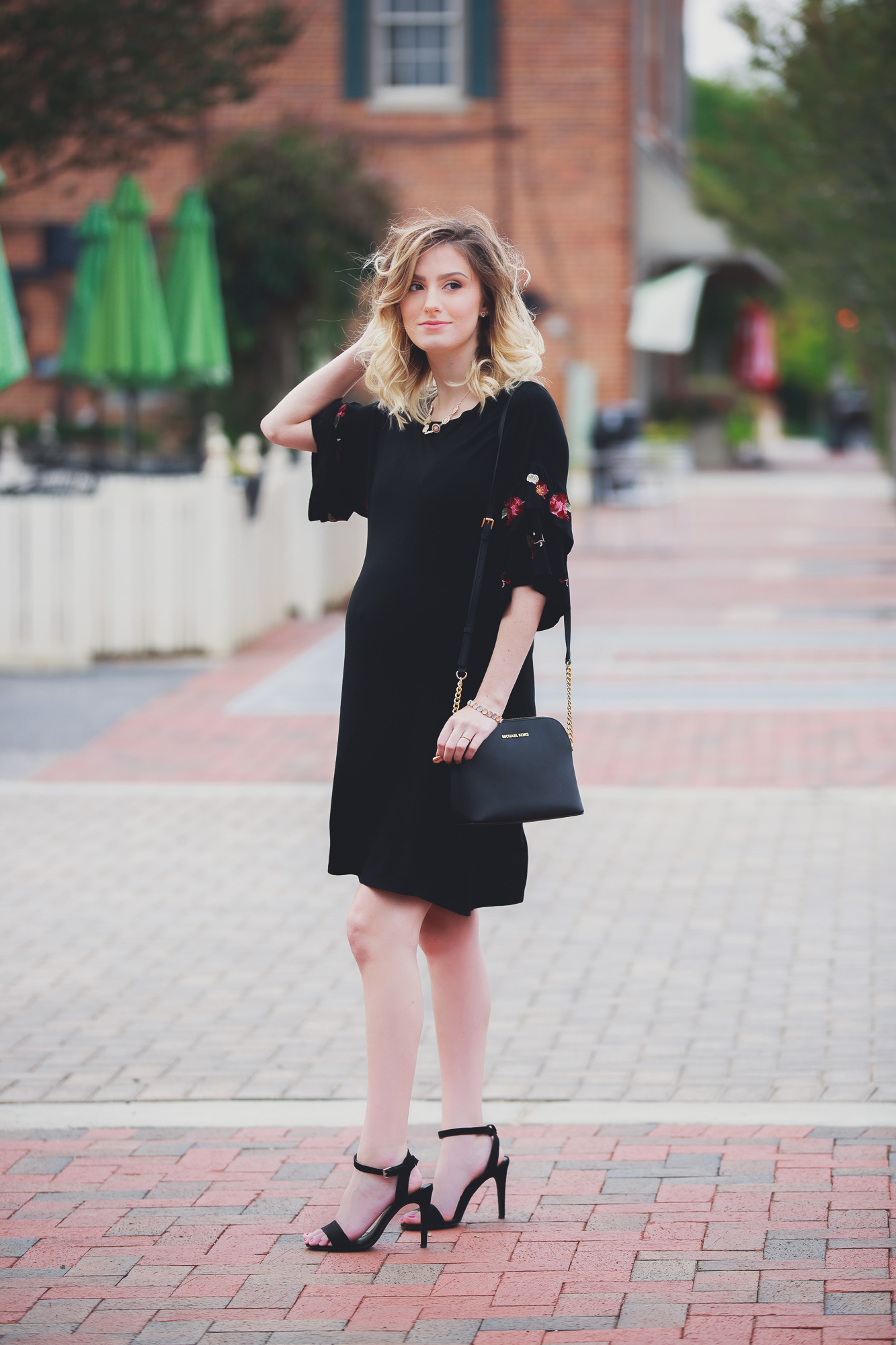 Fashion, lifestyle, and beauty blogger and vlogger Jessica Linn wearing a black ruffle sleeve dress with floral embroidery on the sleeves from Francesca's. Also carrying a Michael Kors purse and black heels from ASOS in Downtown Cary North Carolina.