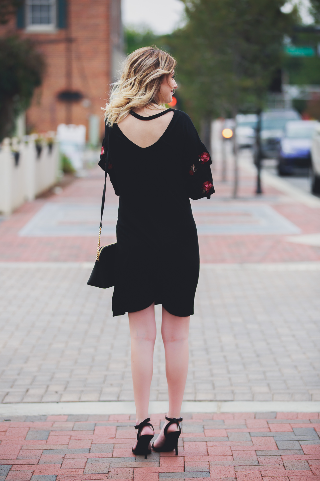 Fashion, lifestyle, and beauty blogger and vlogger Jessica Linn wearing a black ruffle sleeve dress with floral embroidery on the sleeves from Francesca's. Also carrying a Michael Kors purse and black heels from ASOS in Downtown Cary North Carolina.