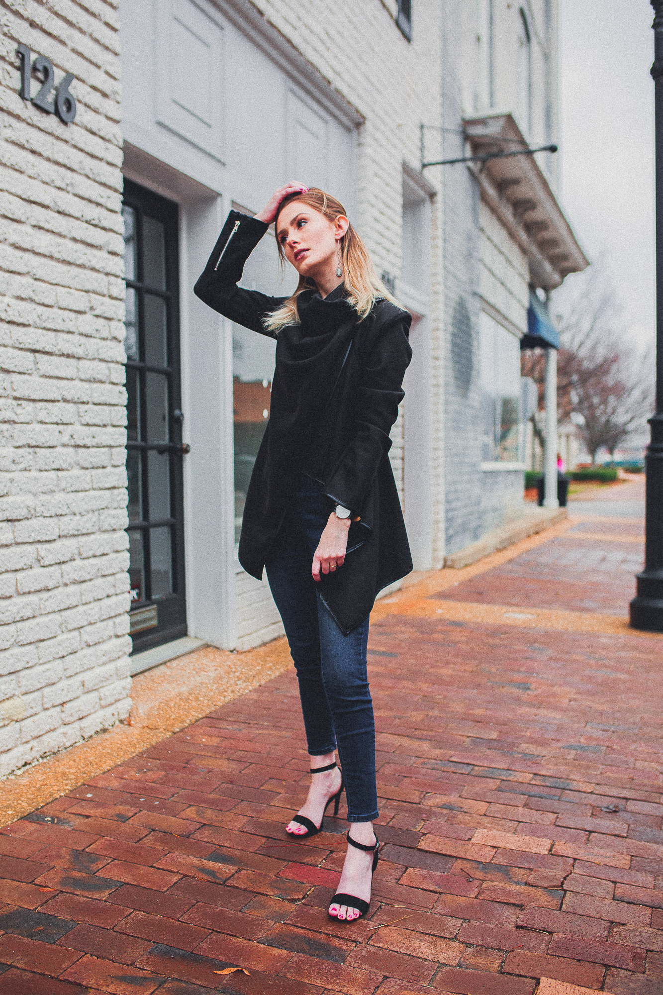 North Carolina fashion and lifestyle blogger Jessica Linn from Linn Style wearing a Welly Merck watch with a black draped coat, dark denim jeans from Target, and black faux suede strappy heels from ASOS. Photography by Joel Pagan taken in Downtown Cary NC