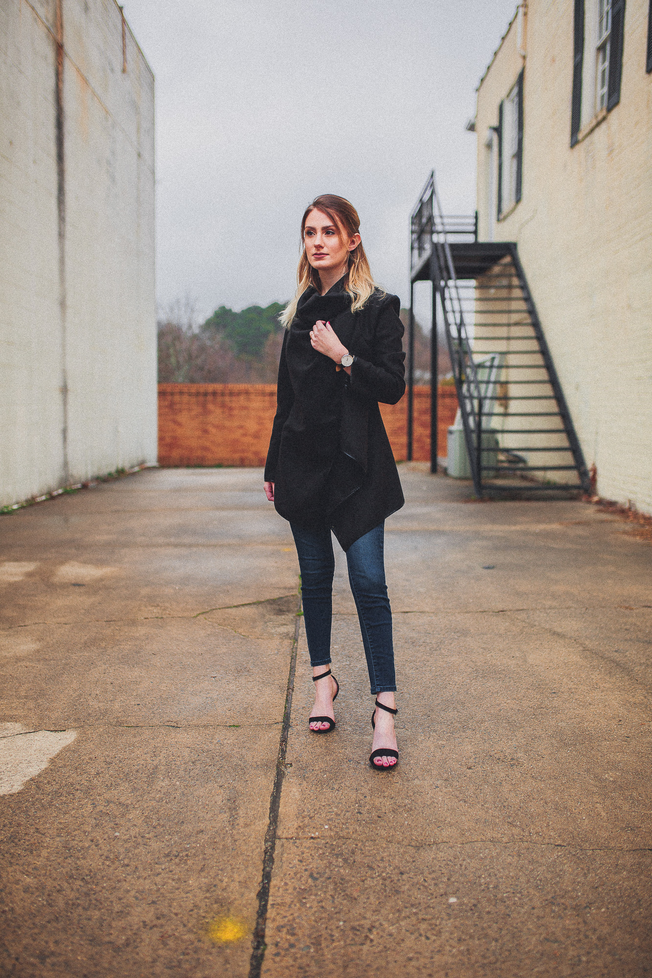 North Carolina fashion and lifestyle blogger Jessica Linn from Linn Style wearing a Welly Merck watch with a black draped coat, dark denim jeans from Target, and black faux suede strappy heels from ASOS. Photography by Joel Pagan taken in Downtown Cary NC