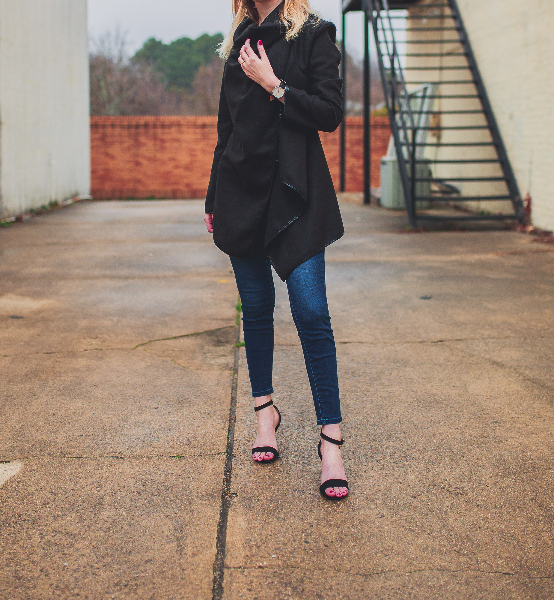 North Carolina fashion and lifestyle blogger Jessica Linn from Linn Style wearing a Welly Merck watch with a black draped coat, dark denim jeans from Target, and black faux suede strappy heels from ASOS. Photography by Joel Pagan taken in Downtown Cary NC