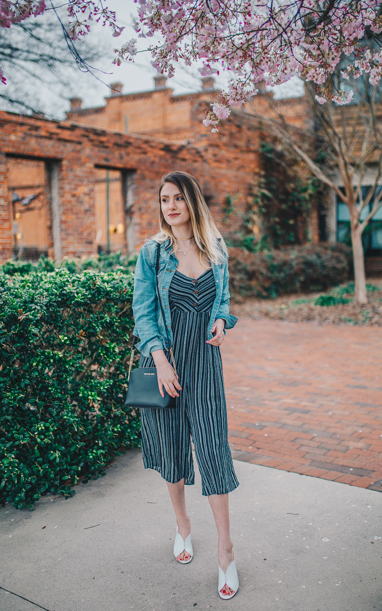 How To Style A Jumpsuit by North Carolina fashion and lifestyle blogger Jessica Linn. Navy blue chevron culotte jumpsuit from Forever21 worn with a denim jacket, white heeled mules from Target Who What Wear, a black Michael Kors Purse from Macy's, a gold chevron choker form Cary NC jewelry store CY Design Studio, and necklace from Copper Bloom. A casual and effortless summer outfit.