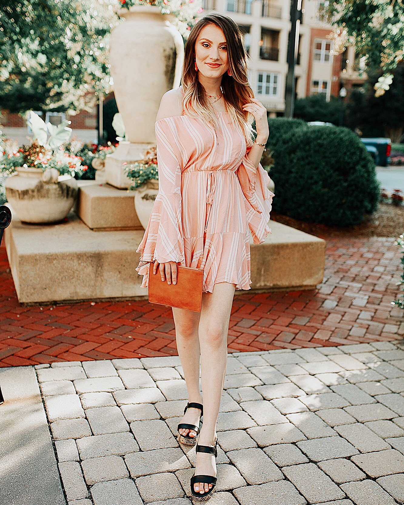Pink bell sleeve romper with white stripes from Copper Bloom, layered tassel necklace from Baublebar, tassel earrings from Siam Hills Tribe, clutch from Anne Taylor. Summer outfit inspiration styles by North Carolina fashion and lifestyle blogger Jessica Linn.