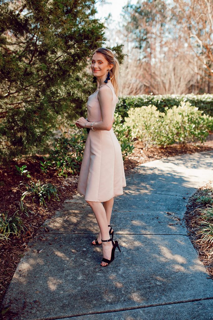 Valentines Day Outfit Inspiration | Kate Spade Fit & Flare Dress by popular North Carolina fashion and lifestyle blogger, Jessica Linn, owner and author or Linn Style and Babies, Love, & Lattes.  Jessica wearing a pale pink fit and flare dress with a black bow on the waist, black sandal heels, and throwing glitter heart confetti.