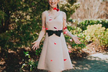 Valentines Day Outfit Inspiration | Kate Spade Fit & Flare Dress by popular North Carolina fashion and lifestyle blogger, Jessica Linn, owner and author or Linn Style and Babies, Love, & Lattes. Jessica wearing a pale pink fit and flare dress with a black bow on the waist, black sandal heels, and throwing glitter heart confetti.
